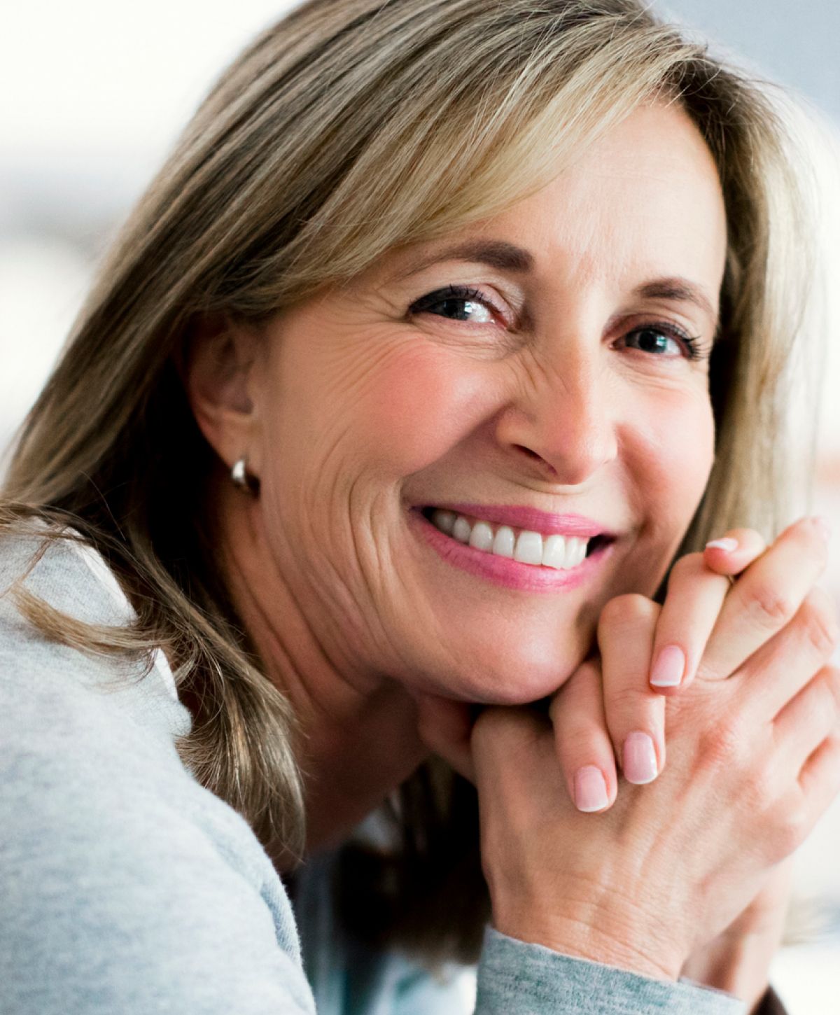 Smiling woman with hands clasped in contemplation.