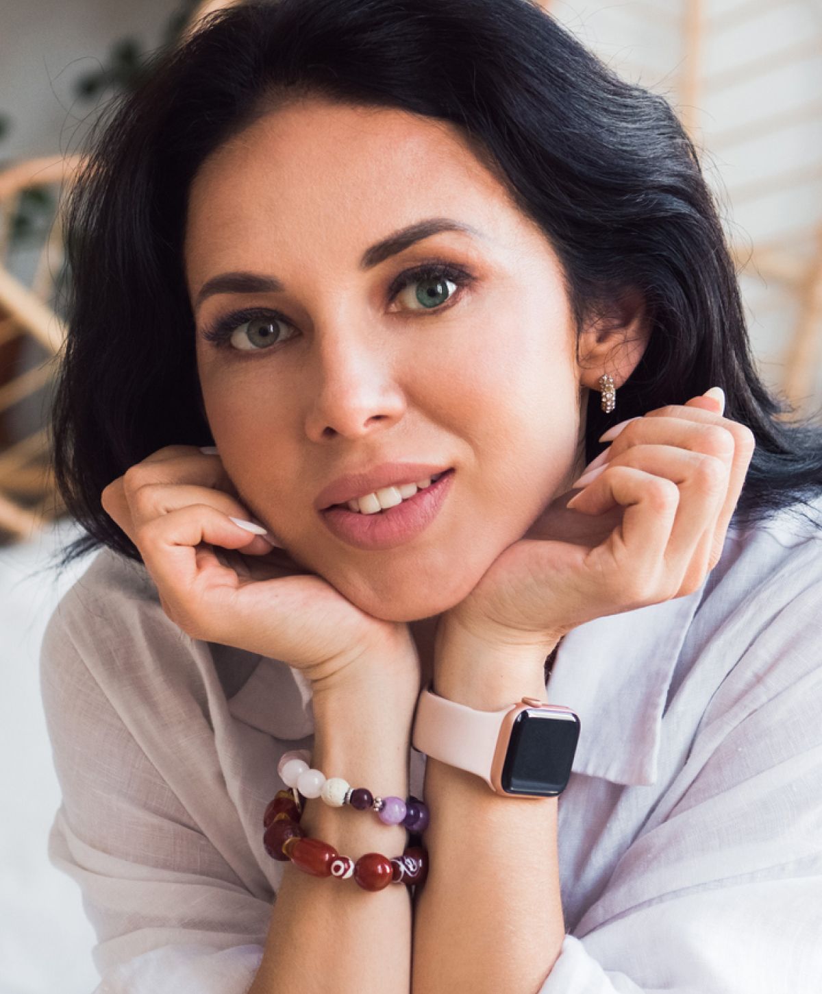 Woman with bracelets and smartwatch, smiling gently.