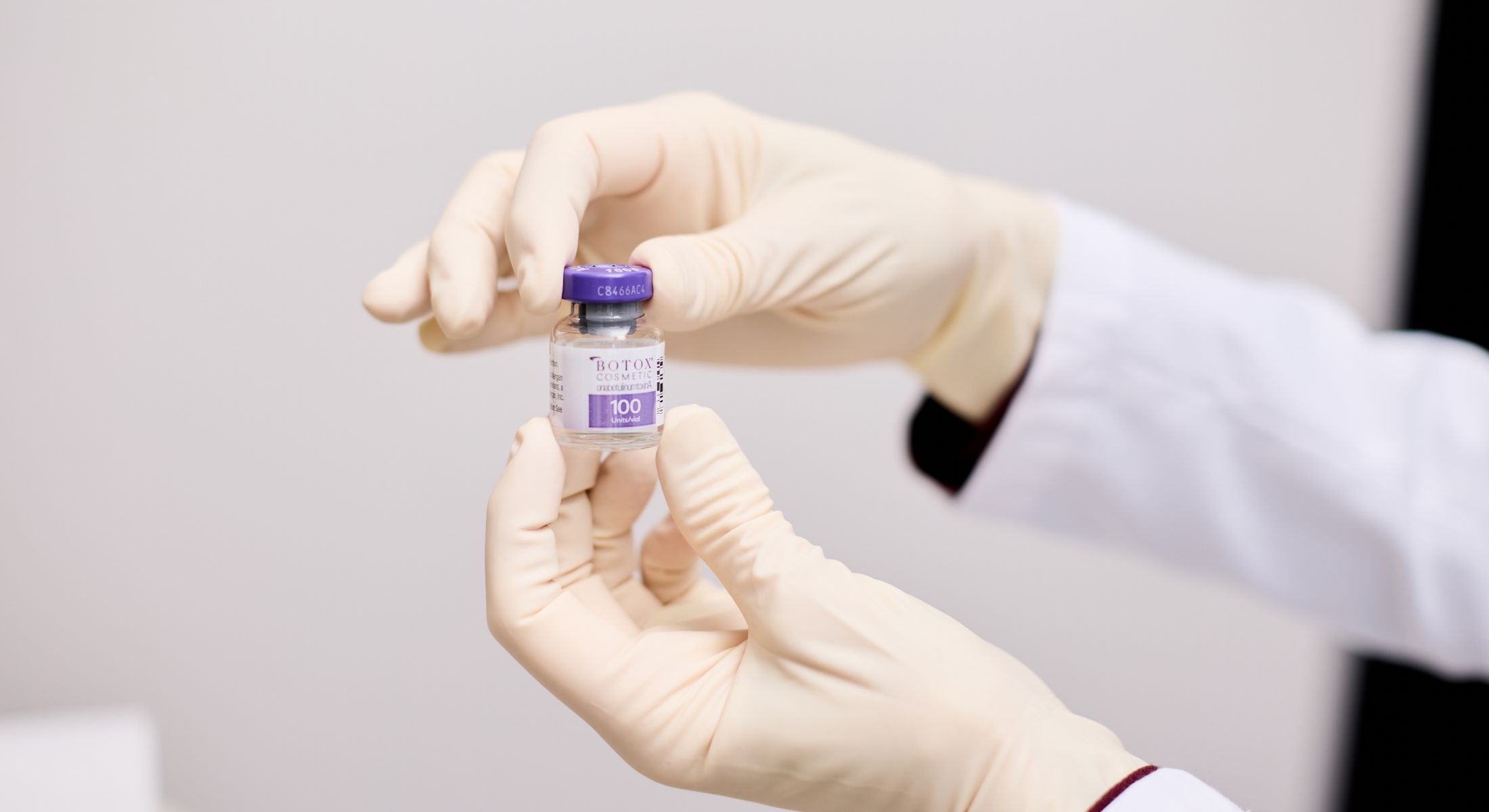 Vial of Botox held by gloved hands.