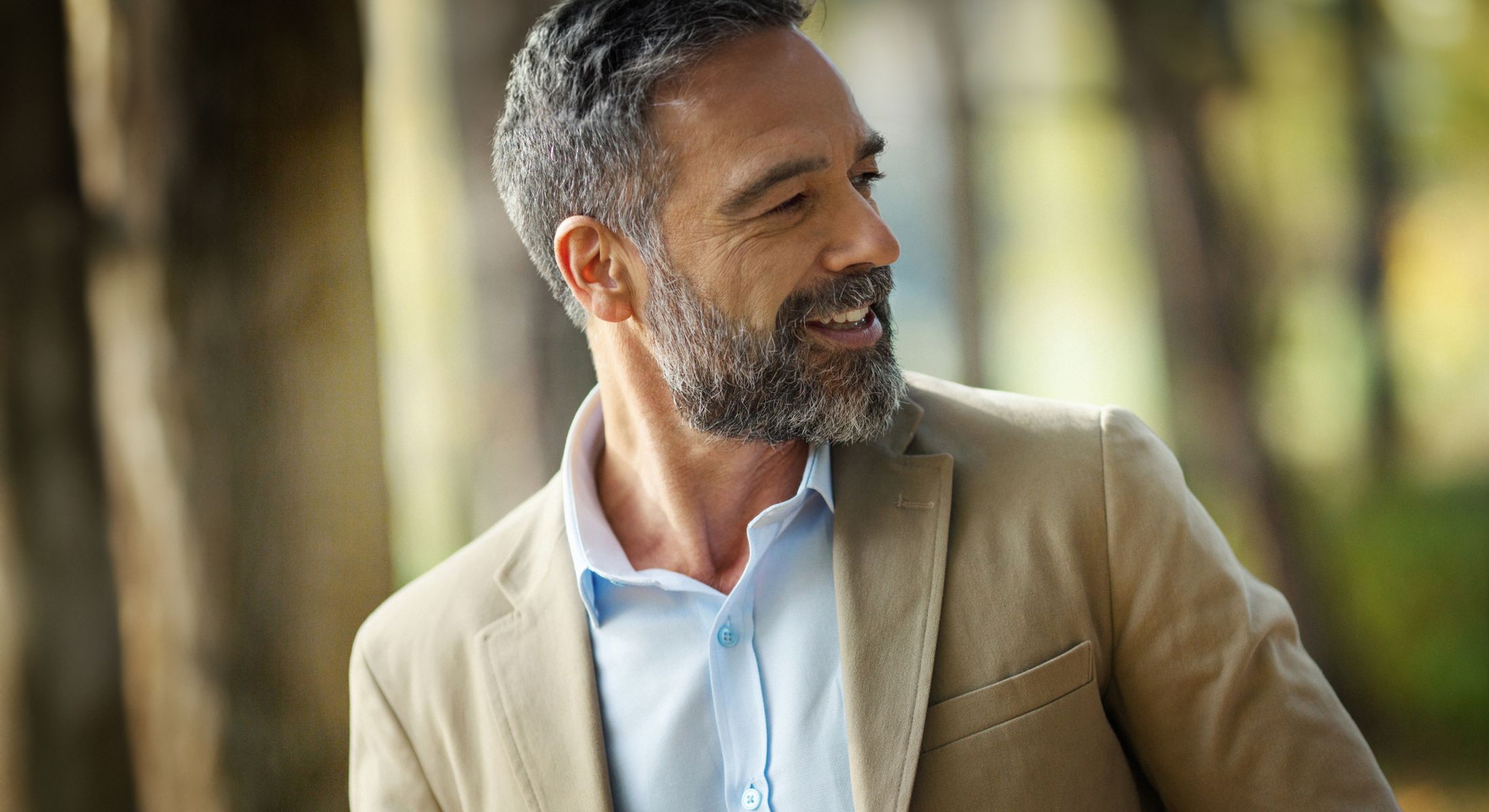 Man smiling in beige blazer outdoors.